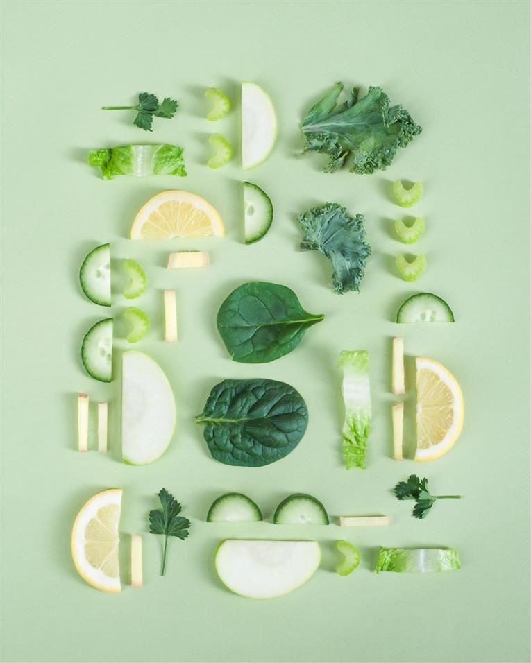 Green fruits and vegetables on light green background, sliced produce arranged in offset blocks