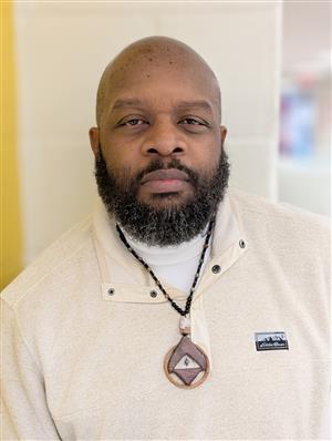 Mr. Hamer, an African-American man with a serious expression, beard &mustache, wearing a sweater, turtleneck and medallion