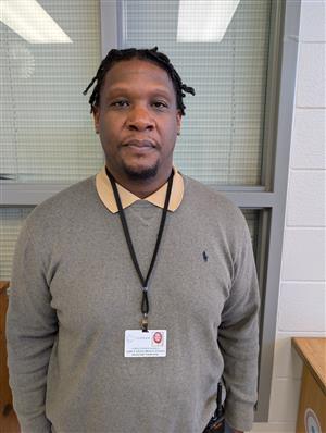 Photo of Mr. Howell, an African-American man with twists, wearing a polo sweater and collared shirt.